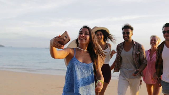女孩用手机欢迎人们在海滩上自拍，快乐微笑的男女朋友