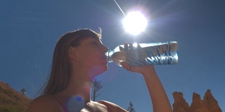 特写:年轻的女旅行者在炎热阳光充足的沙漠中饮水补水