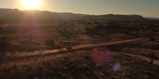 航拍:金色夕阳下，黑色SUV吉普车行驶在沙漠山谷的土路上