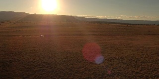 航拍:金色日出时，一辆黑色SUV行驶在沙漠山谷尘土飞扬的道路上