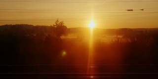 黎明从一列行驶的火车上看到的景象。树木和建筑物的剪影在初升的太阳的背景下迅速闪动