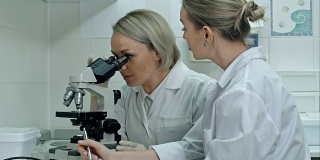 两位年轻的女科学家在现代实验室里用显微镜和笔记写报告