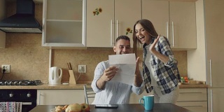 迷人的幸福夫妇在家吃早餐时在厨房收到喜讯展开信