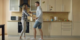 迷人的年轻快乐的夫妇有乐趣跳舞，同时在厨房做饭在家里