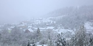雪落在树木繁茂的山脚下的小村庄