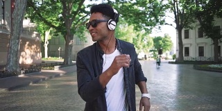 年轻时髦的黑人男子戴着白色耳机和太阳眼镜在市中心的户外跳舞，玩得很开心