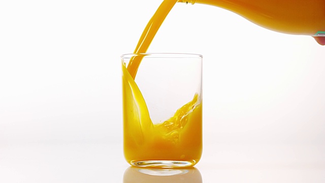 在白色背景下，将橙汁倒入玻璃中，慢动作4K