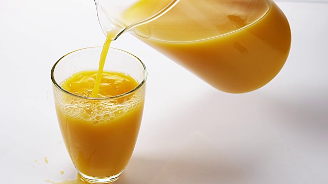 在白色背景下，将橙汁倒入玻璃中，慢动作4K