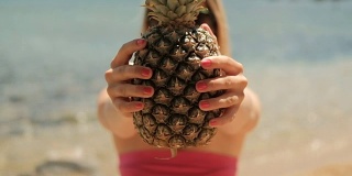 夏天，年轻女子捧着菠萝站在沙滩上