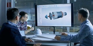 工业工程师小组讨论三维涡轮/发动机部件设计显示在演示显示。在背景工厂被看到。