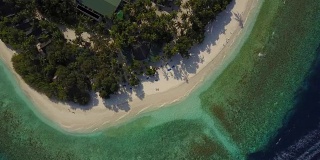 无人机镜头降落到空旷的热带白色沙滩上，只有一对夫妇躺在马尔代夫的环礁岛度假村的躺椅上晒太阳，那里有棕榈树的影子和蓝绿色的印度洋。快艇正驶过。假期的隐私