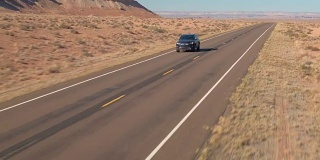 空中特写:一辆黑色SUV行驶在空旷的道路上，穿过广阔的沙漠山谷