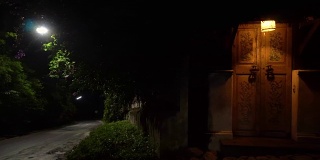 在一个宁静的夜晚，路边有一扇带灯的复古门。晚上全景