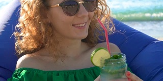 年轻女子在海边享用热带莫吉托鸡尾酒和新鲜的酸橙