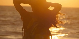 日落时分，年轻的女游客在海边扎马尾辫。日出时，美丽的女孩在海边捏着自己的头发。女背包客编织头发和做发型。护发