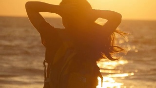 日落时分，年轻的女游客在海边扎马尾辫。日出时，美丽的女孩在海边捏着自己的头发。女背包客编织头发和做发型。护发视频素材模板下载