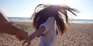 跟着我拍的一个年轻女人拉着她的男朋友在海边。女孩牵着男人的手，在热带异国的海滩上奔向大海。暑假或假期。的观点。观点慢动作