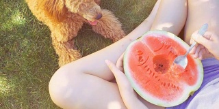 年轻女子和她的狗吃了半个红色的西瓜，放松在院子里。