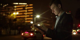 一个年轻人晚上在街上使用他的平板电脑