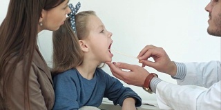 小女孩正在接受男医生用压舌板检查咽喉