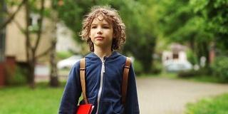 一个10-11岁男孩放学回家的肖像。在他身后，他背着一个背包，手里拿着一个红色文件夹。他脸上的表情严肃而专注