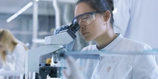 医学研究科学家检查实验室小鼠和在显微镜下观察组织样本。她在一个灯光实验室工作。