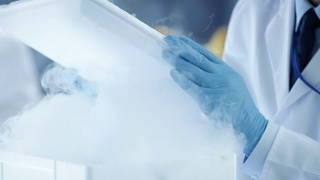 一个医学研究科学家打开冰箱盒子拿出有样品的培养皿并检查它的特写。他在一个繁忙的现代化实验室中心工作。视频素材模板下载