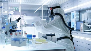 医学病毒学研究科学家工作在一个危险防护服与口罩，她从冰箱盒子拿出试管和使用微管。她在一个无菌的高科技实验室工作，研究设施。视频素材模板下载