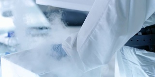 医学病毒学研究科学家工作在防护服和口罩，她检查试管与分离病毒串从冰箱盒子。她在一个无菌的高科技实验室/研究机构工作。
