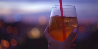 那个女孩正端着一杯鸡尾酒。橙汁透明饮料加冰。年轻的河流和一个大酒杯对着日落。一个浪漫的夜晚。软焦点