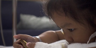 婴儿女儿在病床上使用智能手机的特写。年轻病人的放松时间。治疗室实时拍摄。