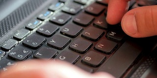 一个男人的手在一个黑色笔记本电脑键盘键上打字的特写。