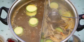 概念火锅亚洲料理。把蘑菇和西葫芦从沸腾的汤中取出，用撇油加酱