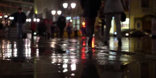 雨夜，在路灯的照耀下，雨点落在五颜六色的沥青上。不认识的人在雨伞下走，过有红绿灯的马路。美丽的彩色的散景。天气、交通、城市街道、现代城市生活方式的概念