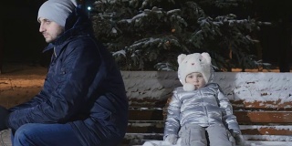 争吵的父母和女儿坐在冬季公园的长椅上