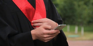 男毕业生在智能手机上看问候视频，查看社交网络