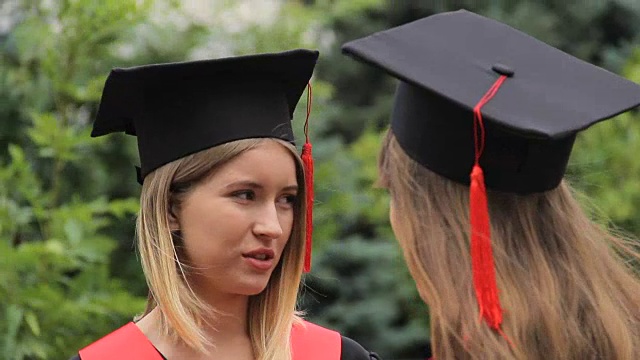 两名女毕业生在毕业典礼后穿着学术服装交谈