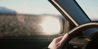 在美丽的日落下的乡村沙漠道路上的汽车内的景色。男性的手在轮子上的特写视图