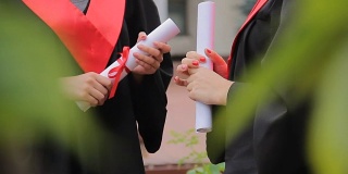 女毕业生拿着毕业证书系着红丝带聊天