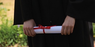 毕业生手中拿着毕业证书系着红丝带，毕业了