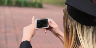 快乐学生戴着毕业帽在智能手机上拍摄朋友，过节