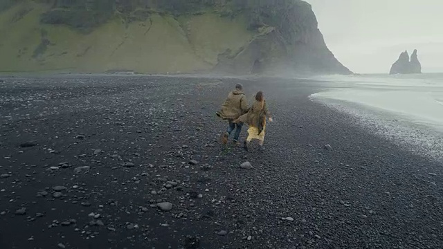 这对年轻的潮人夫妇在冰岛巨怪脚趾附近的黑色火山海滩上跑步