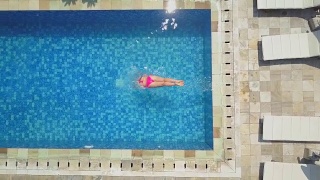 航拍:一个穿着粉色比基尼泳装的女孩跳进豪华度假村的空游泳池里视频素材模板下载