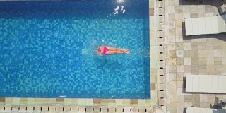 航拍:一个穿着粉色比基尼泳装的女孩跳进豪华度假村的空游泳池里