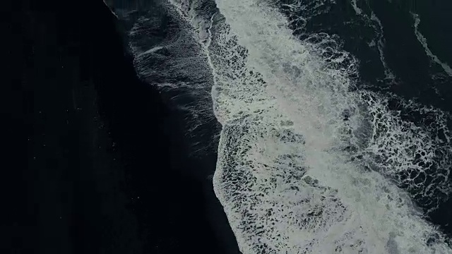 鸟瞰图的强大的波浪与泡沫来海岸上的黑色火山海滩在冰岛