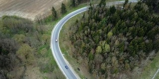 无人机拍摄的乡村公路附近的绿色森林。汽车从岔路口穿过