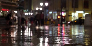 抽象背景雨后的城市在自然的黑暗色调。在街灯的照耀下，雨点落在五颜六色的沥青上。在人群中，两个朋友打着伞聊天。现代城市生活方式