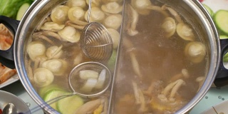 概念火锅家庭烹饪。用撇子从沸腾的汤中取出西葫芦。鱿鱼在回收船