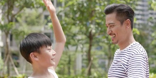 亚洲父亲和儿子欢呼得分在户外篮球运动在早上