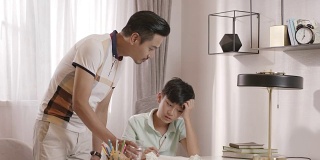 一位亚洲父亲走进阅览室，和儿子聊天，儿子正在做作业